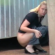 A blonde, Eastern-European girl pees behind a shipping container.